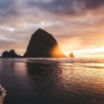 Dramatic sunset over a rocky coastline with wet sand.