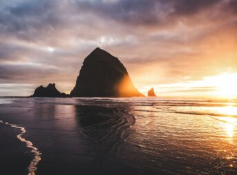 Dramatic sunset over a rocky coastline with wet sand.