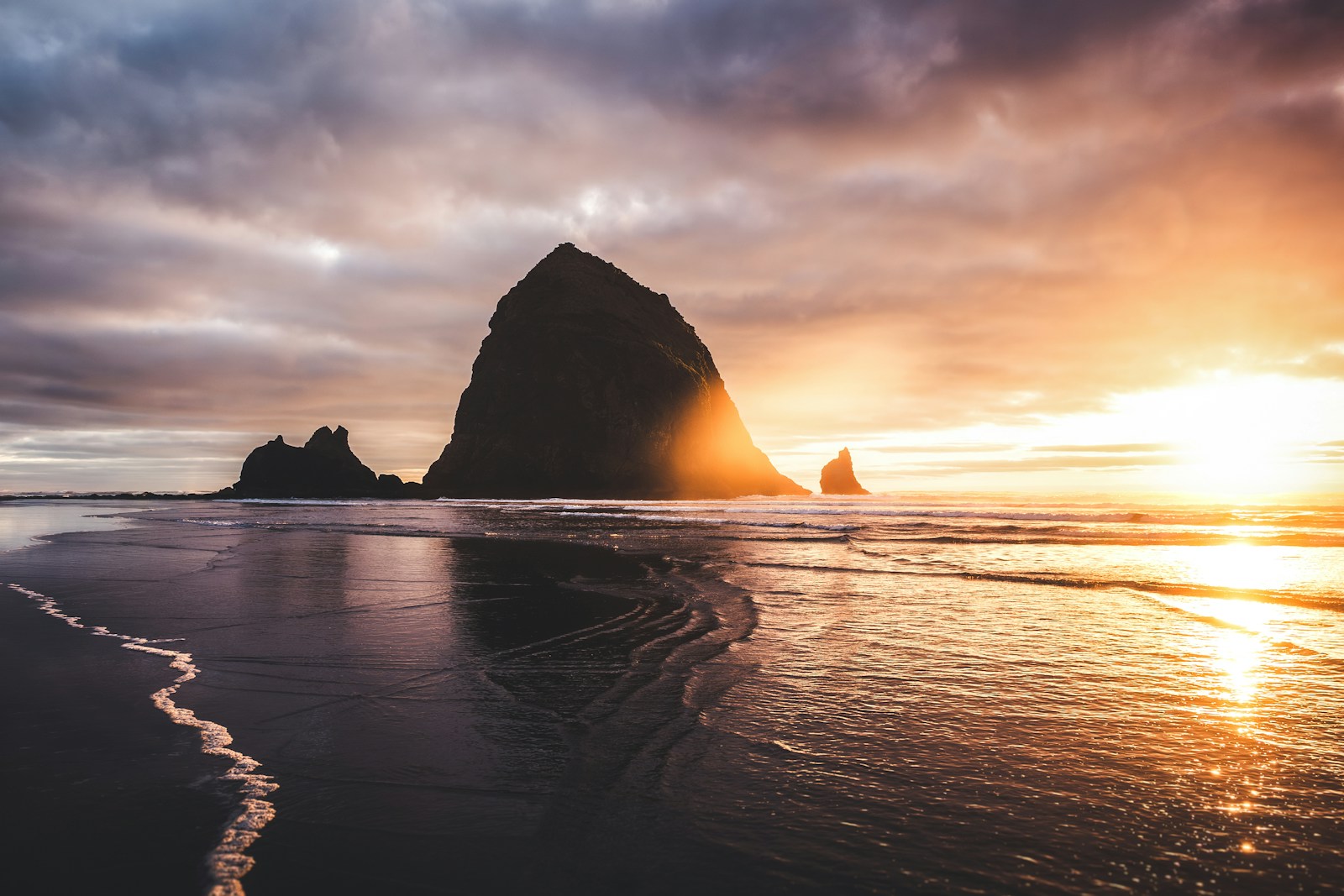 Dramatic sunset over a rocky coastline with wet sand.